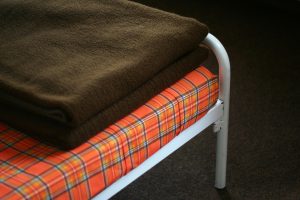 A simple bed, looking 60's/70's style. Brown blanket, orange-brown checked mattress.