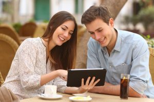Happy couple watching media in a tablet in a restaurant terrace